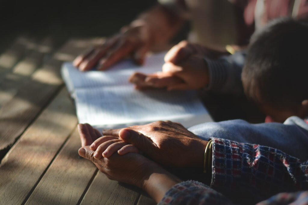 Family members clasp hands over an open Bible in prayer, reflecting Sherman Dumas's guidance in Family Matters on covering yourself and loved ones in protection