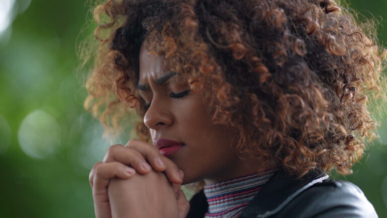 Woman with clasped hands and closed eyes in quiet listening prayer, capturing this practical guide to hearing God's voice from Biblical Prophecy and When God Speaks